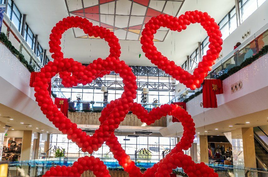 Das Bild zeigt vier herzförmige, riesige Rahmen im Geschosszwischenraum eines Einkaufszentrums, die mit vielen roten Luftballons umkleidet sind.