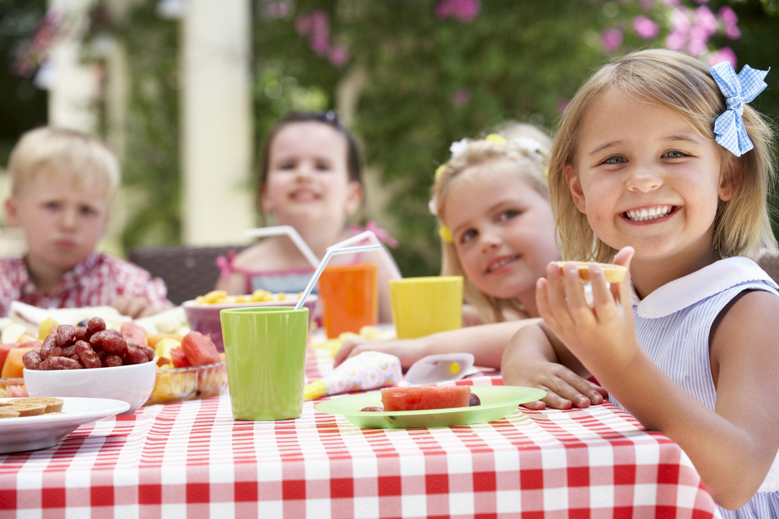 Auf dem Bild sind 4 kinder, 2 Jungen und 2 Mädchen zu sehen, die an einem gedeckten Tisch sitzen und Kuchen essen und sich darüber freuen und lachen.