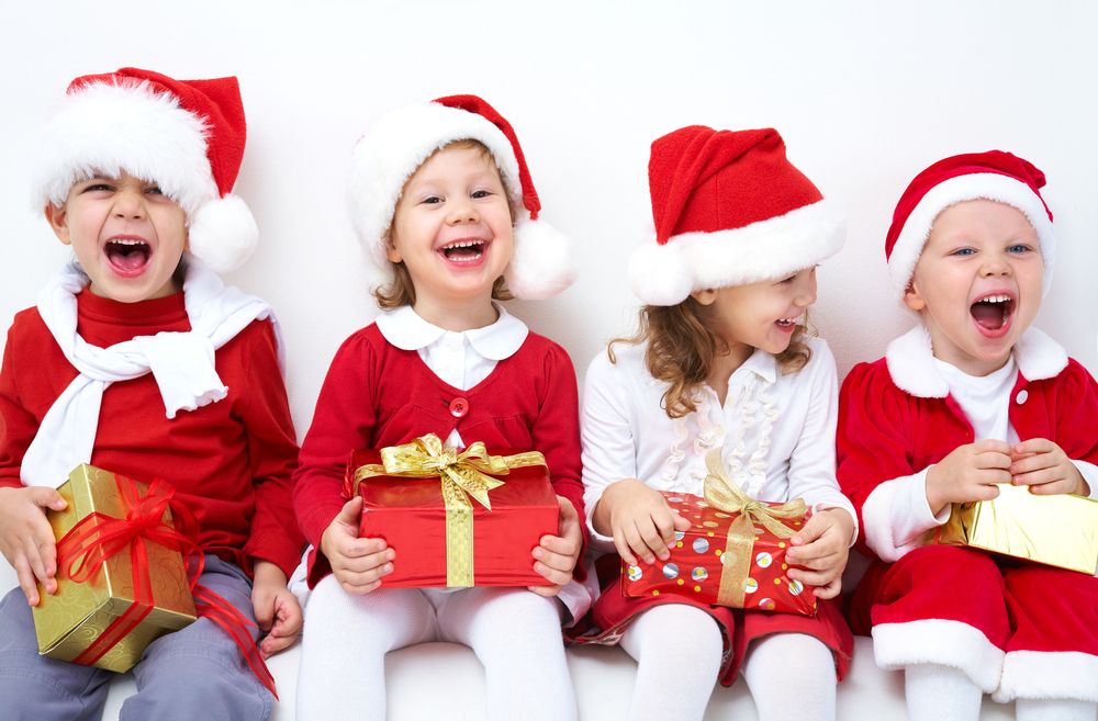 Vier kleine Jungen und Mädchen sind als Nikolaus verkleidet und halten Geschenke in der Hand