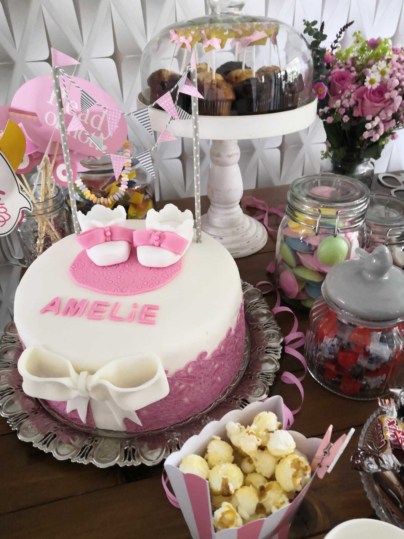 Das Bild ist ein Foto von einer Geburtstagstorte mit Creme und pinkner Verzierung von Namen Amelie mit zwei Babyschuhen Verzierung