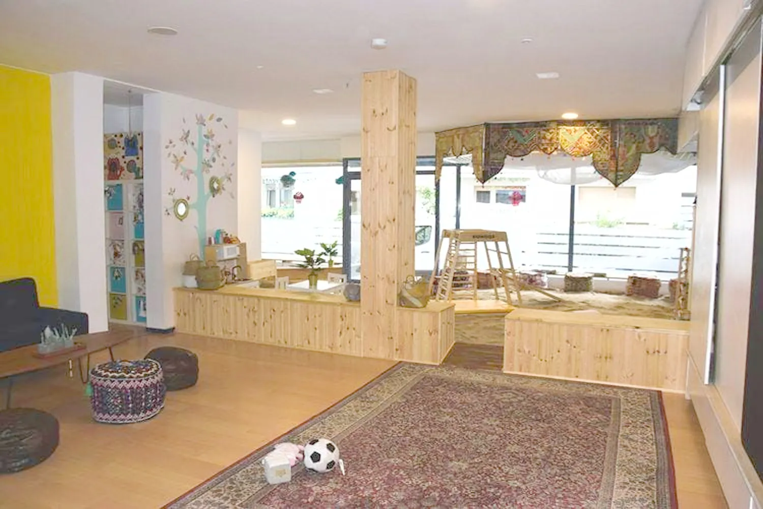 Auf dem Bild ist der Sandraum zu sehen mit Klettergerät, Kindertisch mit Stühlen, Kinderküche und im Hintergrund das Bällebad