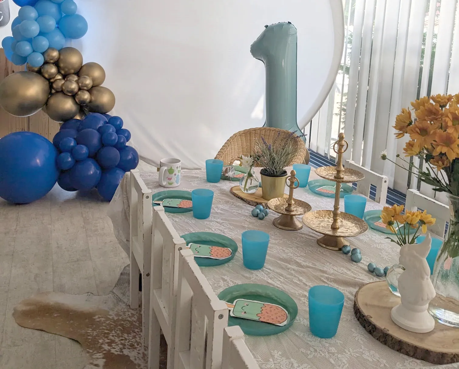 Auf dem Bild ist ein gedeckter Tisch für Kinder zu sehen auf dem Sandboden des Indoor-Sandspielplatzes und im Hintergrund ein Ballonarrangement.